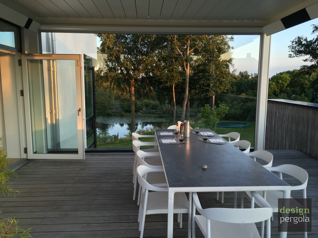 Spiseplads under Camargue Skye pergola i Holte med stort glasværn og udsigt til træer og vand