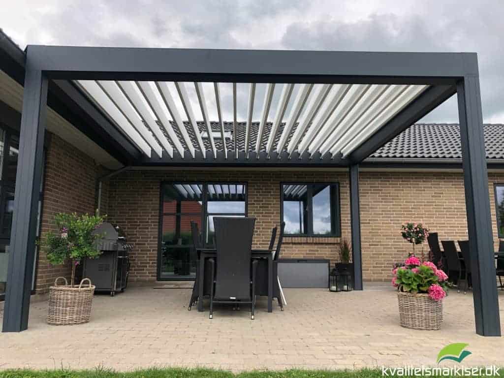 Pergola med åbne lameller over sort spisebord ved et gult murstenshus i Viborg