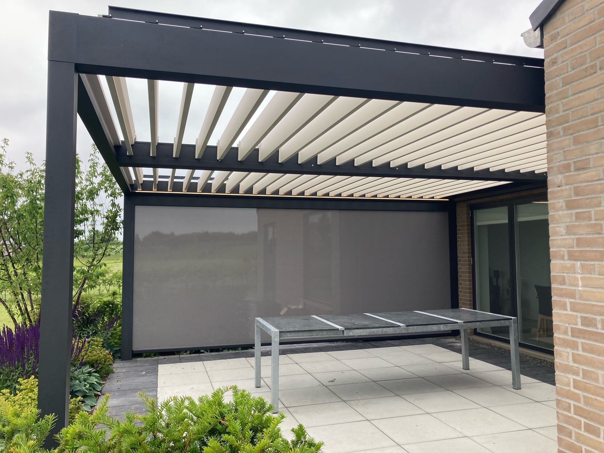 Pergola med elektrisk motor monteret i Randers Pergola med åbne lameller, tændt LED-belysning og nedrullet zipscreen