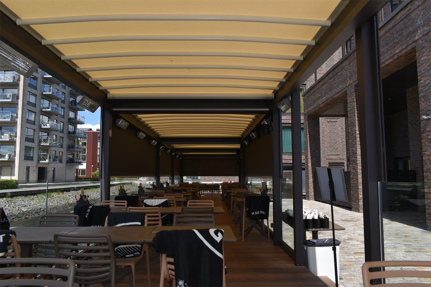 Restaurantborde under lyse tekstiltage med varmelamper og glasværn ved havnefronten i Vejle