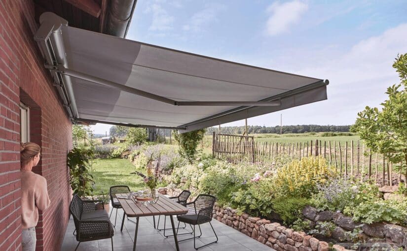 WAREMA Terrea H60 halvkassettemarkise med grå dug, knækarme og forkantflæse over terrasse ved murstenshus.