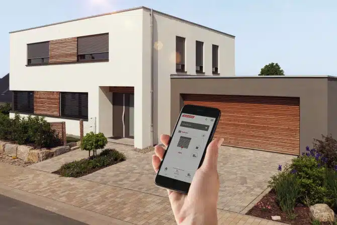 Smartphone med betjening af solafskærmning foran en bolig