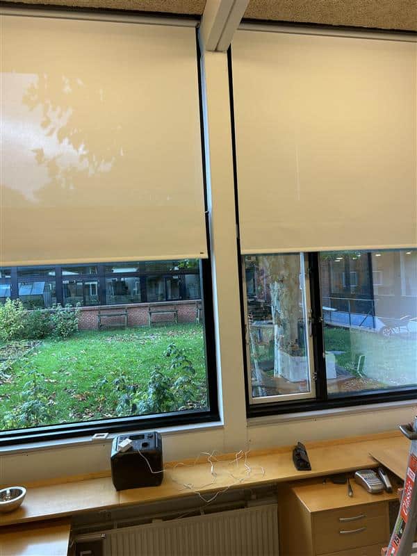 Faber screen-rullegardiner i lokale på skole på Fyn To lyse Faber screen-rullegardiner delvist sænket foran vinduer i et lokale på en skole på Fyn