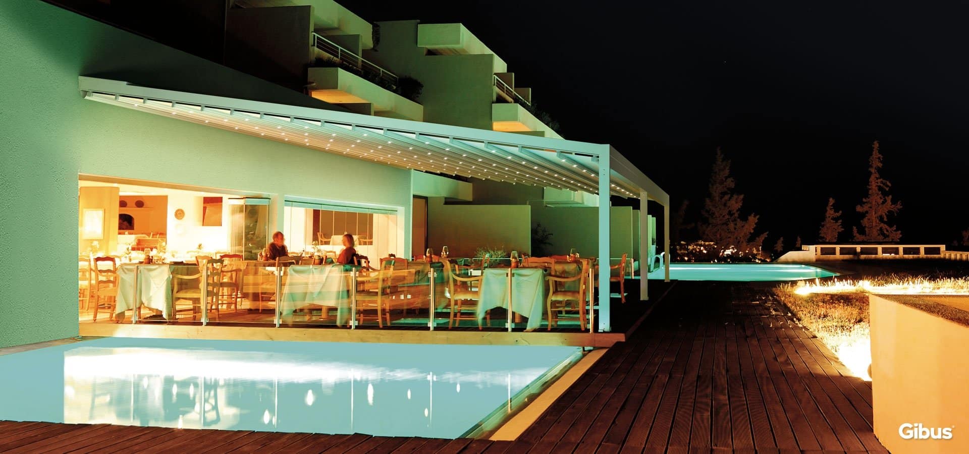 Quadra 165 med belyst tekstiltag og glas omkring en restaurantterrasse ved en pool