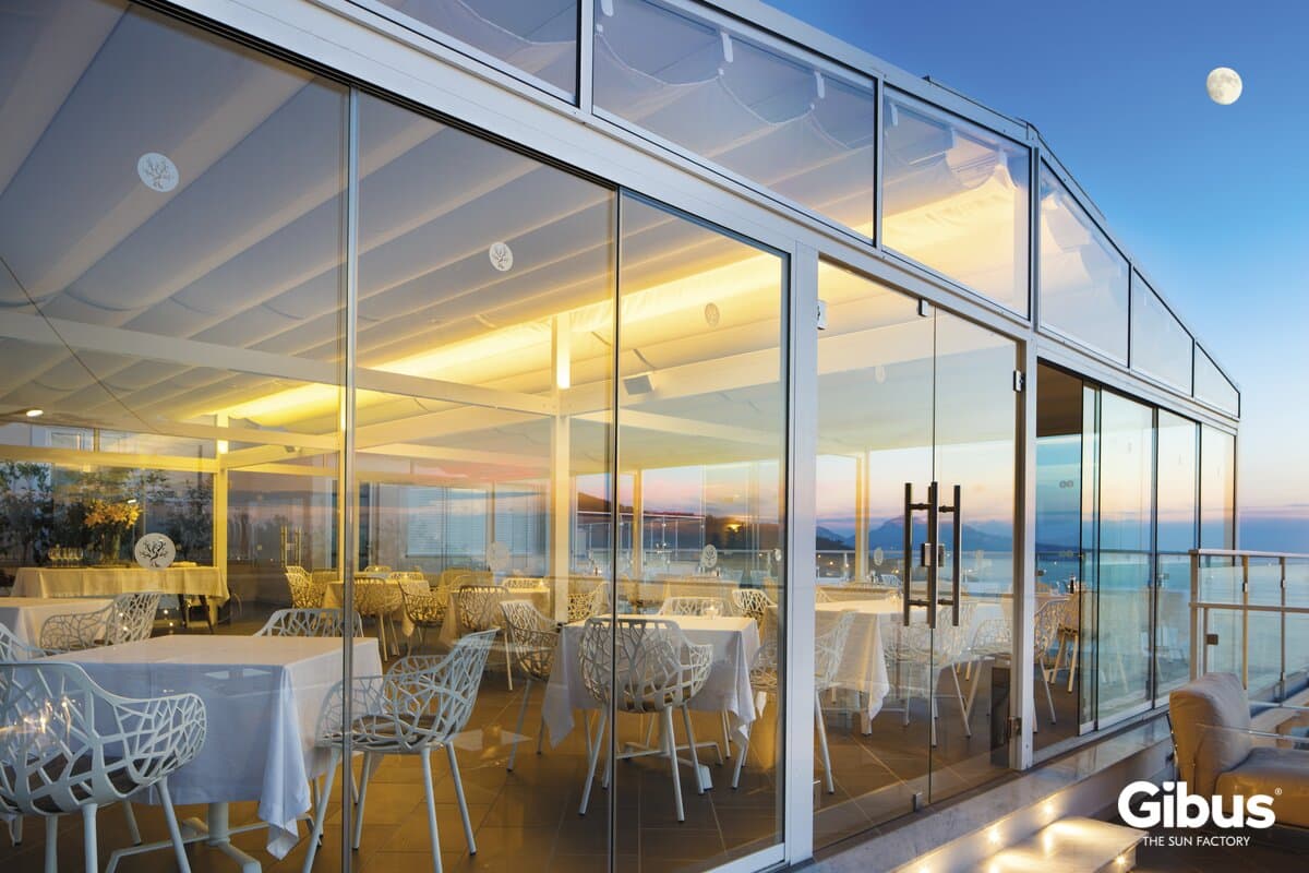 Stor Quadra Pavilion med glaspartier omkring restaurantborde ved havet