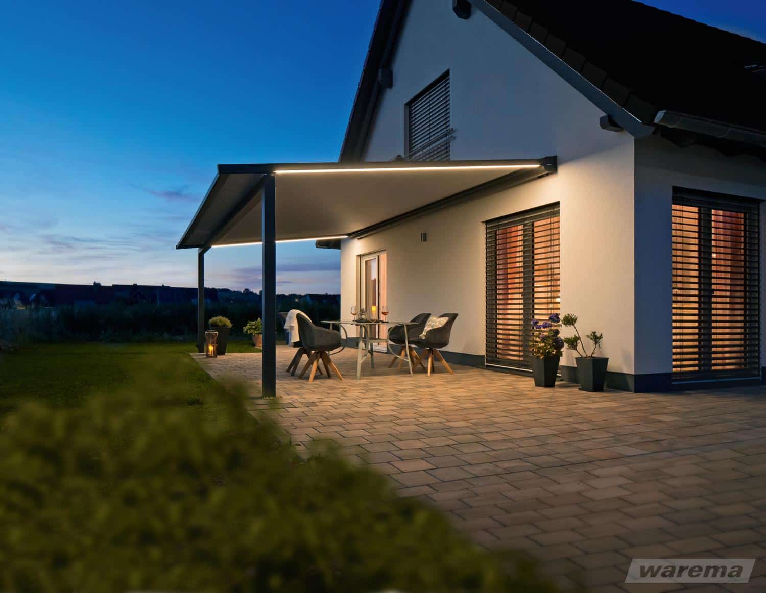 Perea P60 med varm LED-belysning ved et hvidt hus om aftenen