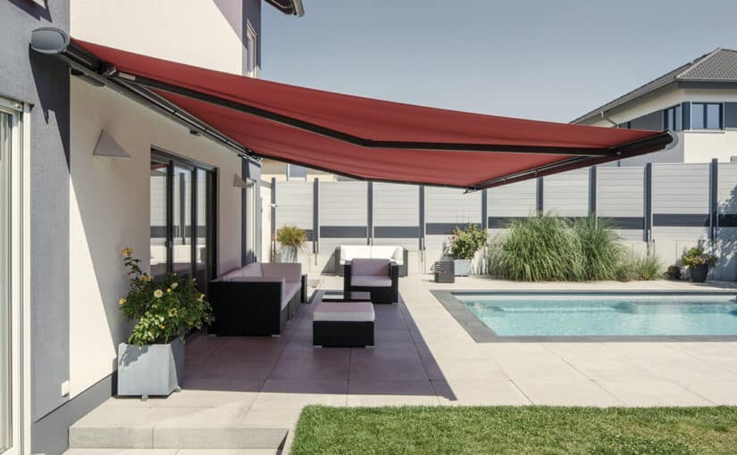 Stor Opal Design II kassettemarkise fra Weinor med mørkt grå stel og rød dug over loungeområde på terrasse og med pool i baggrunden