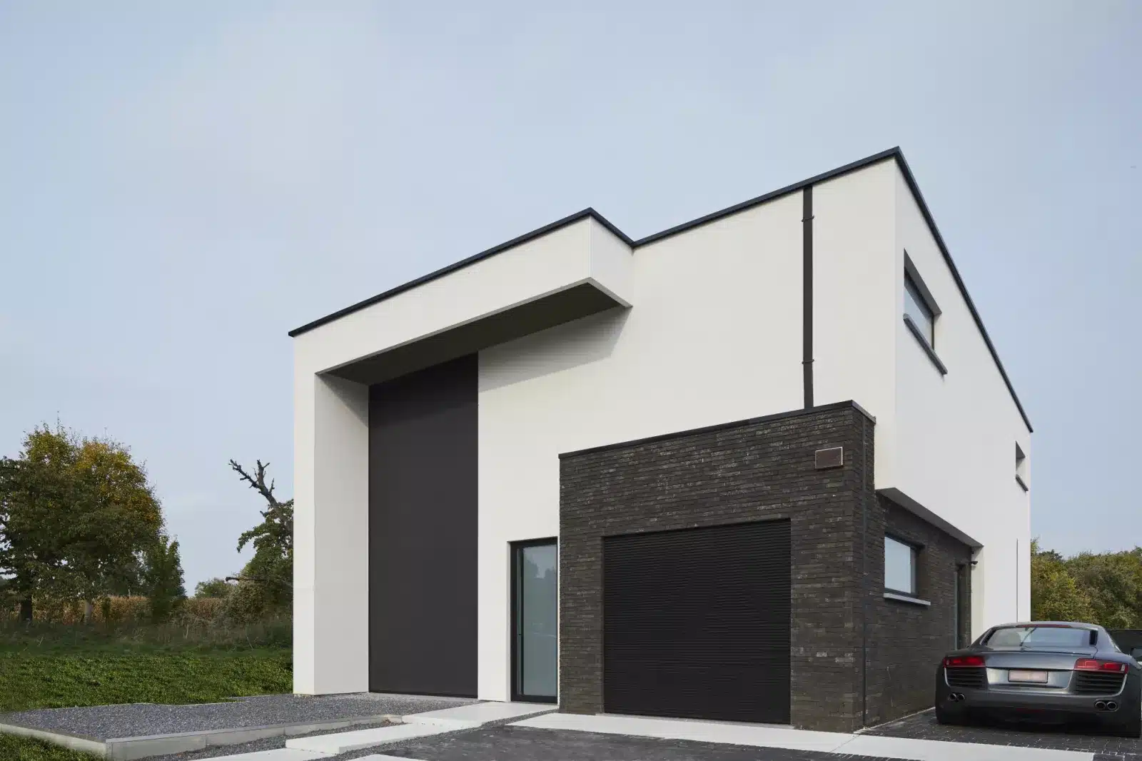 Moderne hus med hvid facade, mørke mursten og en høj Wilms screen foran et stort vinduesparti